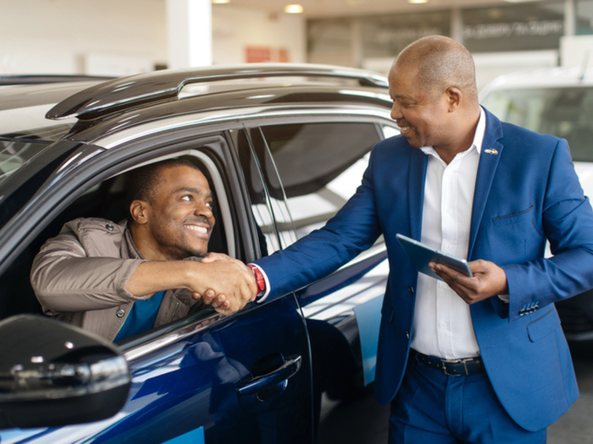 Business owner shaking hands with car dealer after choosing a new commercial vehicle, highlighting insurance cost considerations for Sandbox clients.