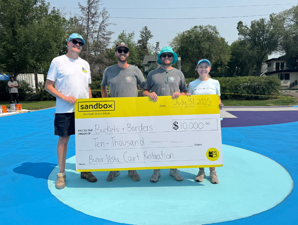 Four people stand behind a large cheque for $10,000 from Sandbox to Buckets and Borders.