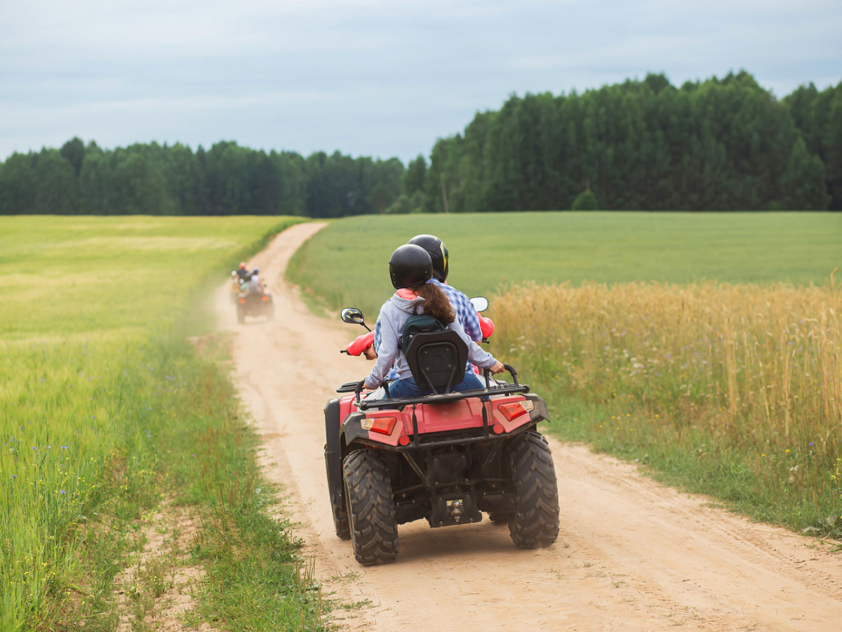 Two riders on a red ATV cruising down a scenic rural dirt trail during a group ride.