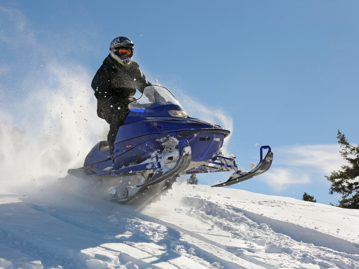 Snowmobile rider traversing a snow-covered hillside with snow spraying behind.