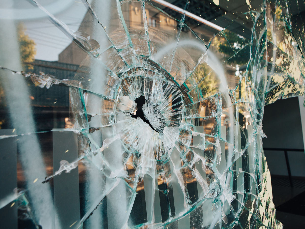 Large hole in a broken storefront window following an act of Vandalism