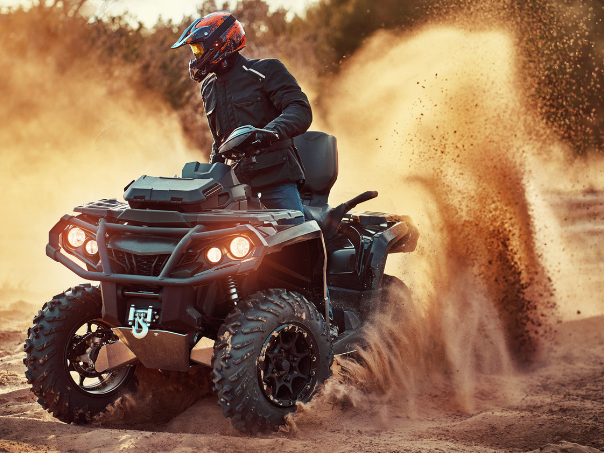 ATV rider wearing a helmet kicking up sand while off-roading in a desert environment.