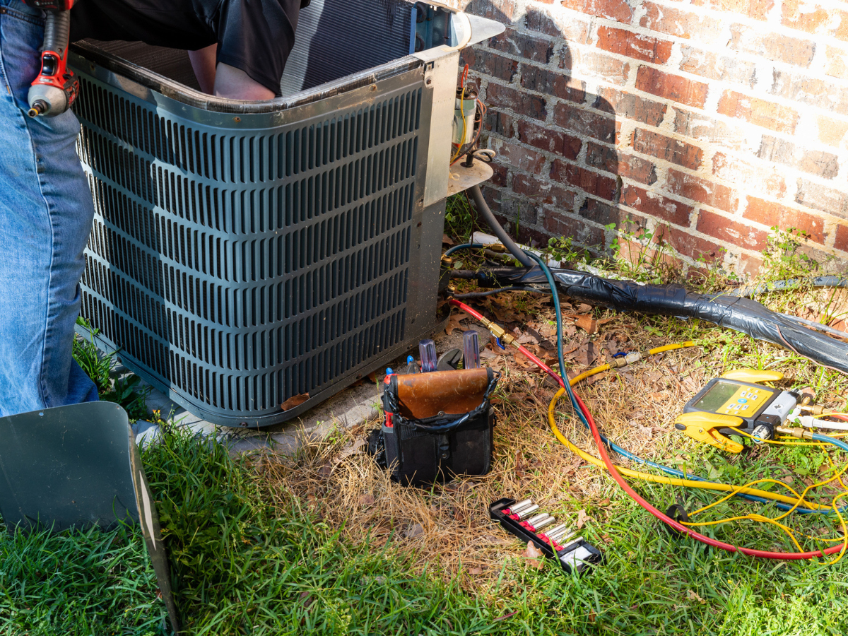 Technician servicing an outdoor HVAC unit beside a brick home