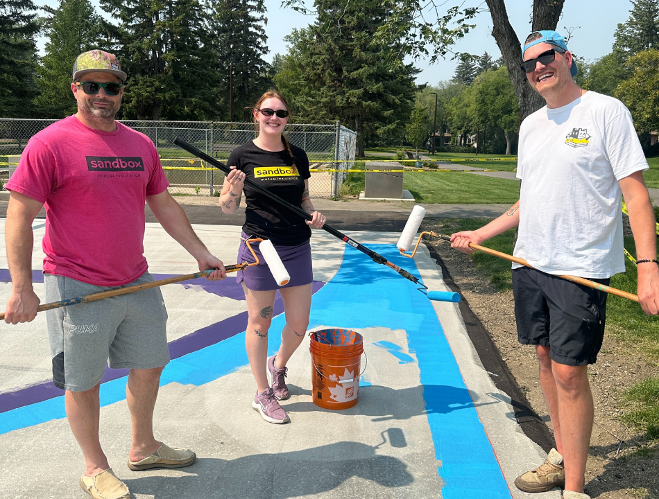 Two men and one woman work together to paint the basketball court.