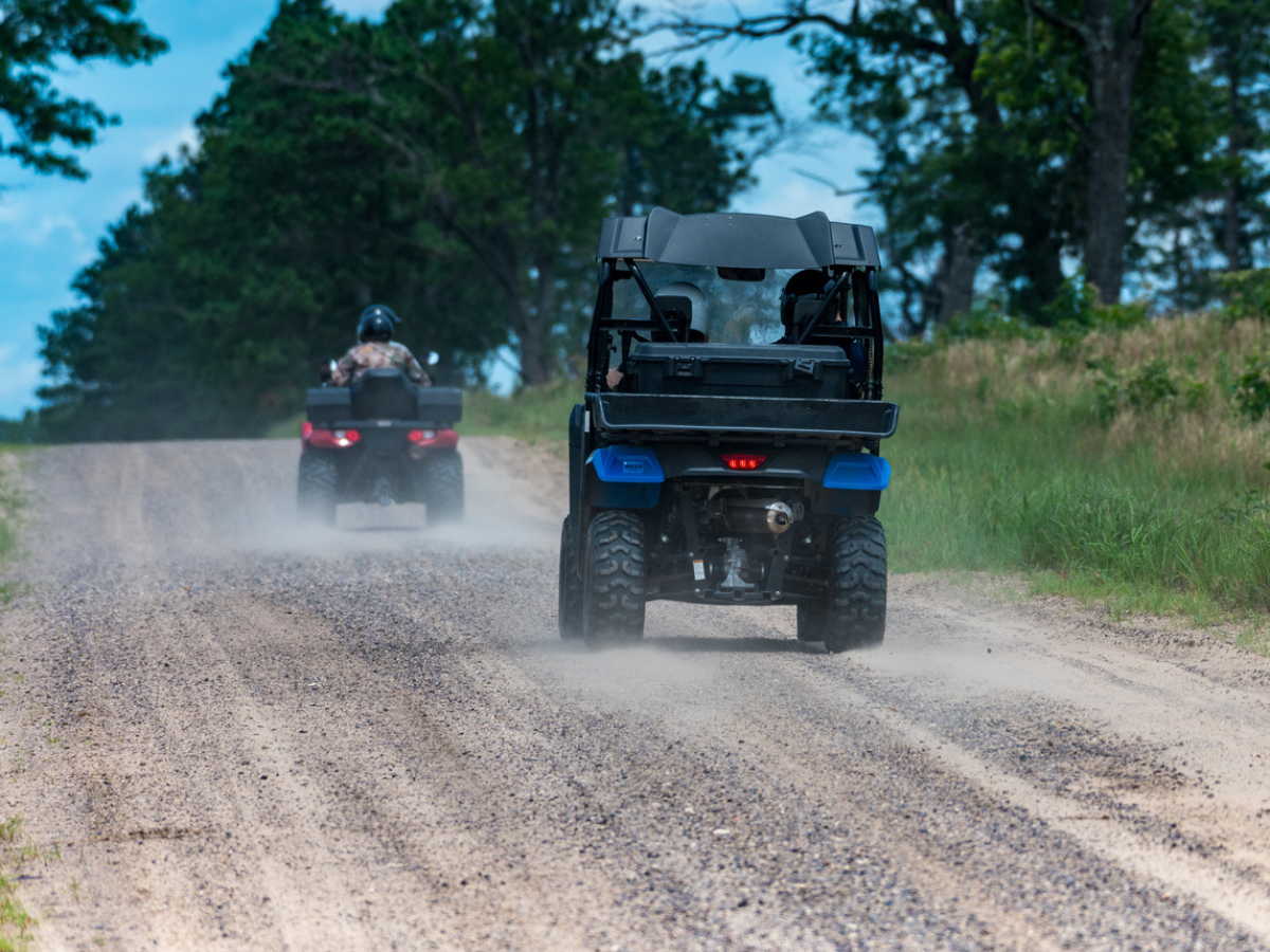 Group of people driving ATVs and UTVs down a dusty rural gravel road during an outdoor adventure.