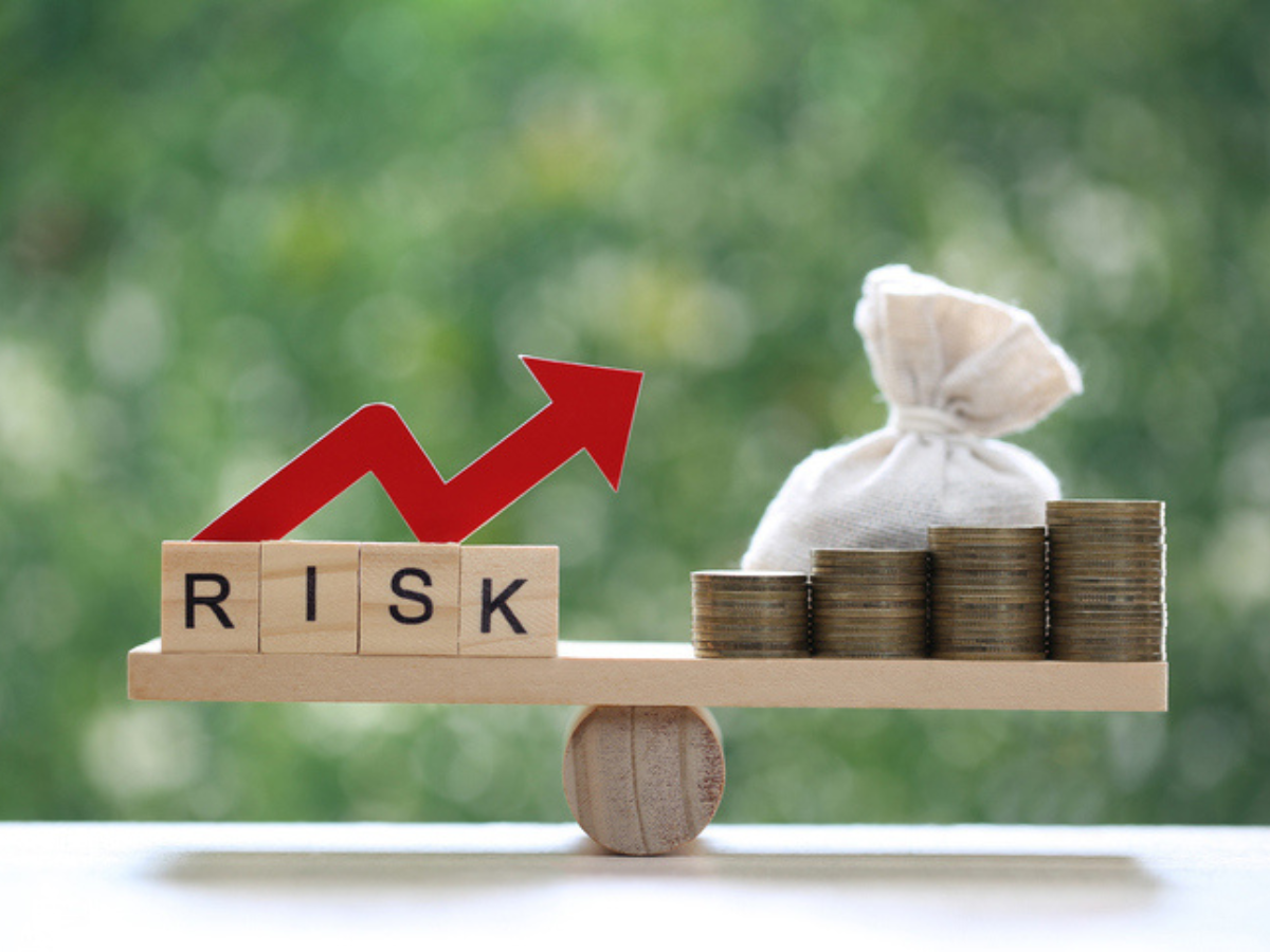 A wooden seesaw with a “risk” block balanced against a money bag, illustrating business risk and insurance protection.