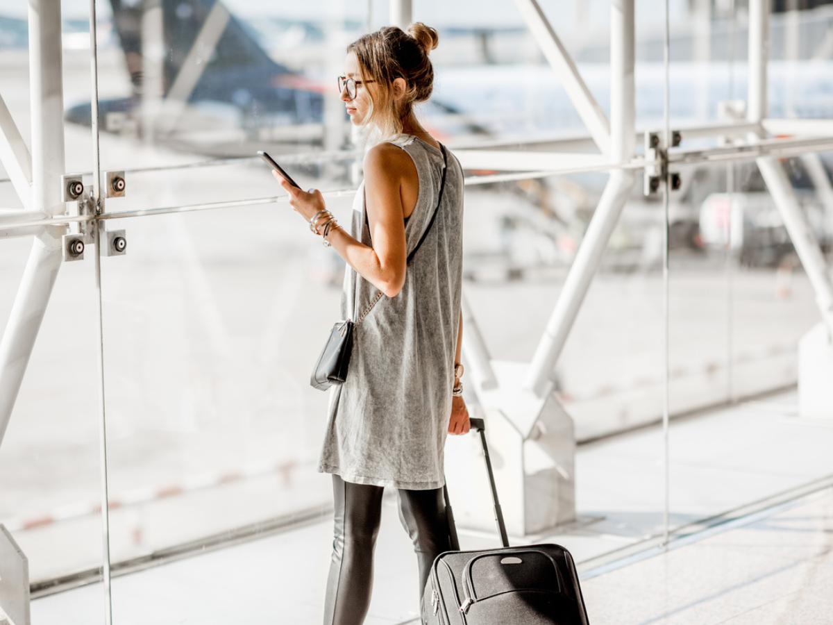 Person standing in an airport with carry-on luggage and a mobile phone.