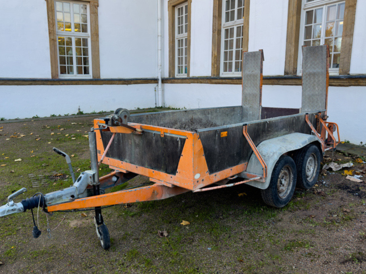 Small orange utility cargo trailer with loading ramps parked beside a building