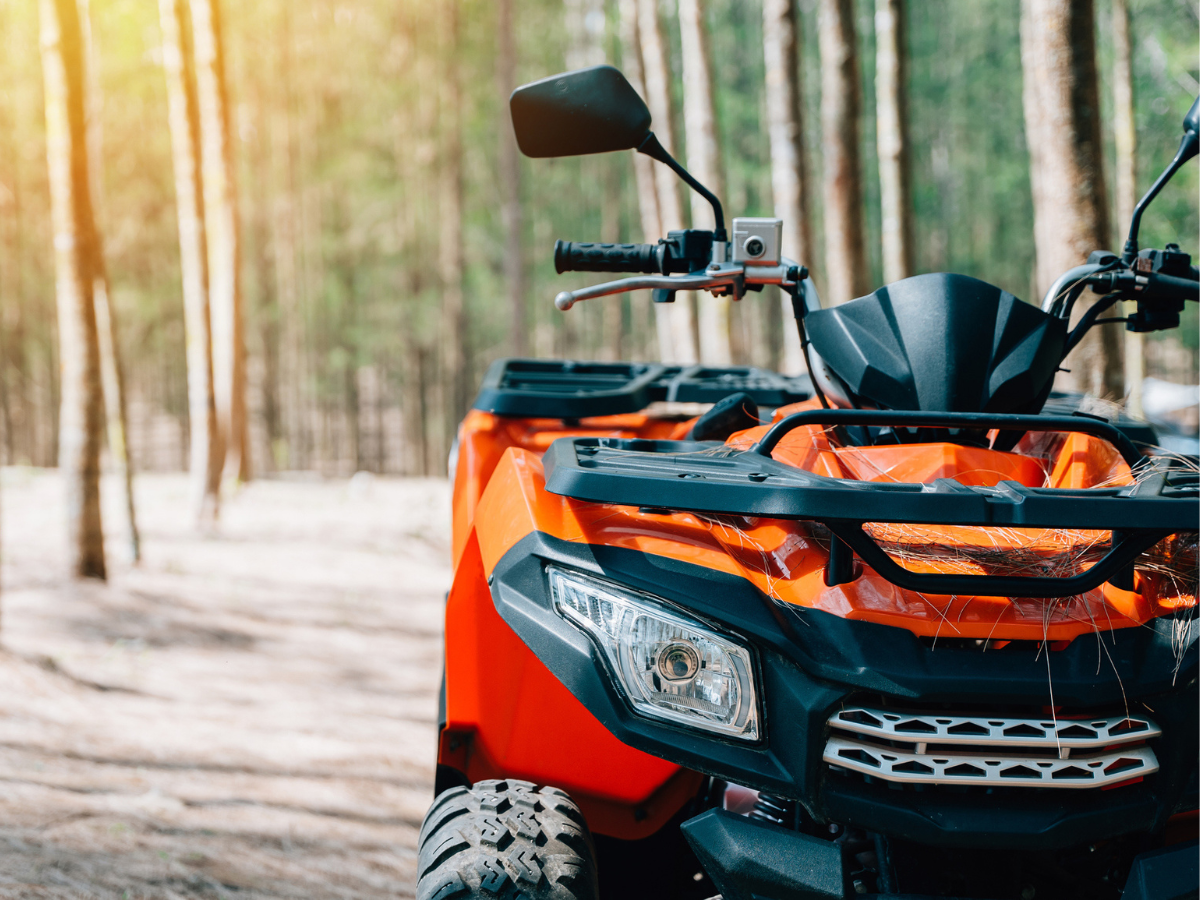 Orange ATV parked on a forest trail, showcasing rugged design for outdoor recreation and off-road adventures