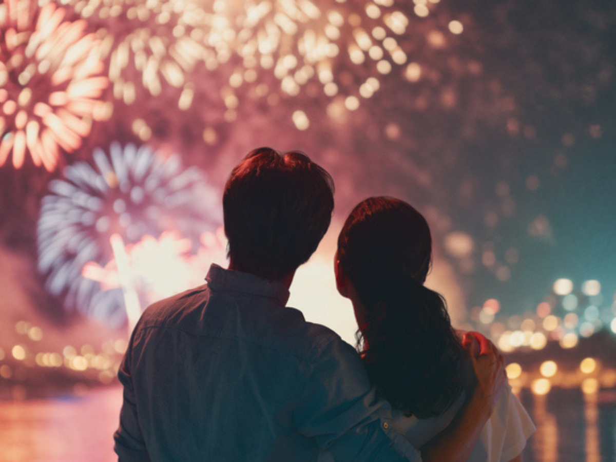 People watching a colorful Firework display over the water at night.