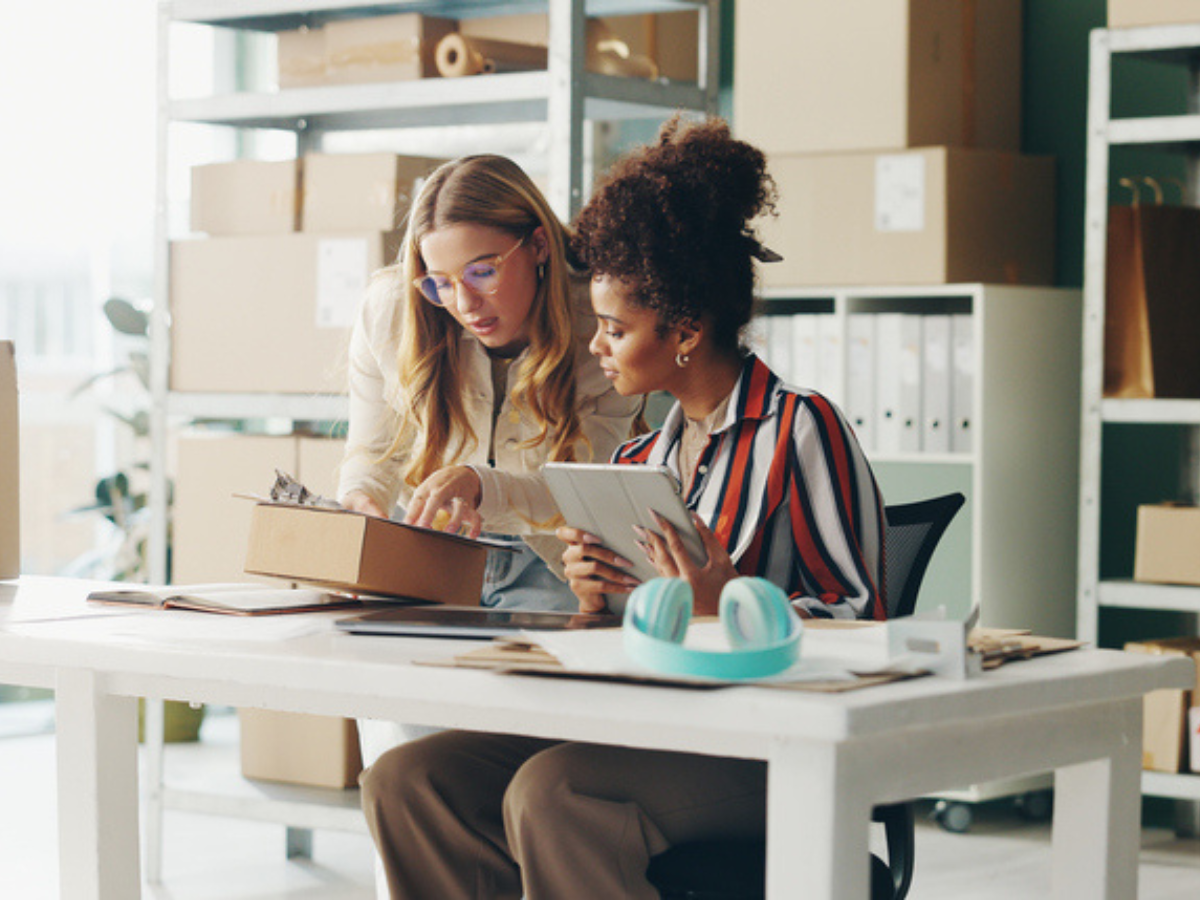Two small business owners reviewing a package and digital tablet in their workspace, representing the importance of business insurance for small businesses.