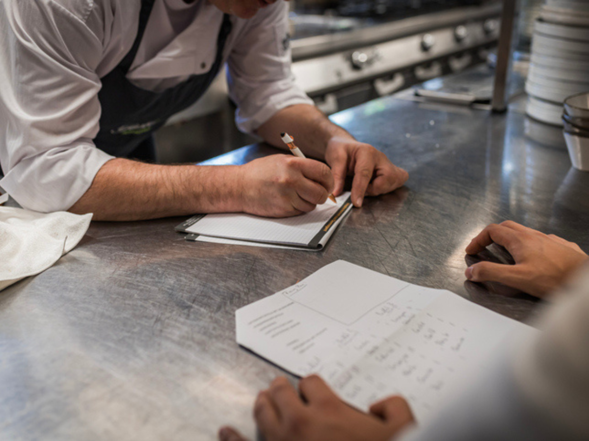 Person writing on a piece of paper, highlighting the process of customizing an insurance plan tailored to a restaurant's specific needs, with a focus on restaurant insurance.
