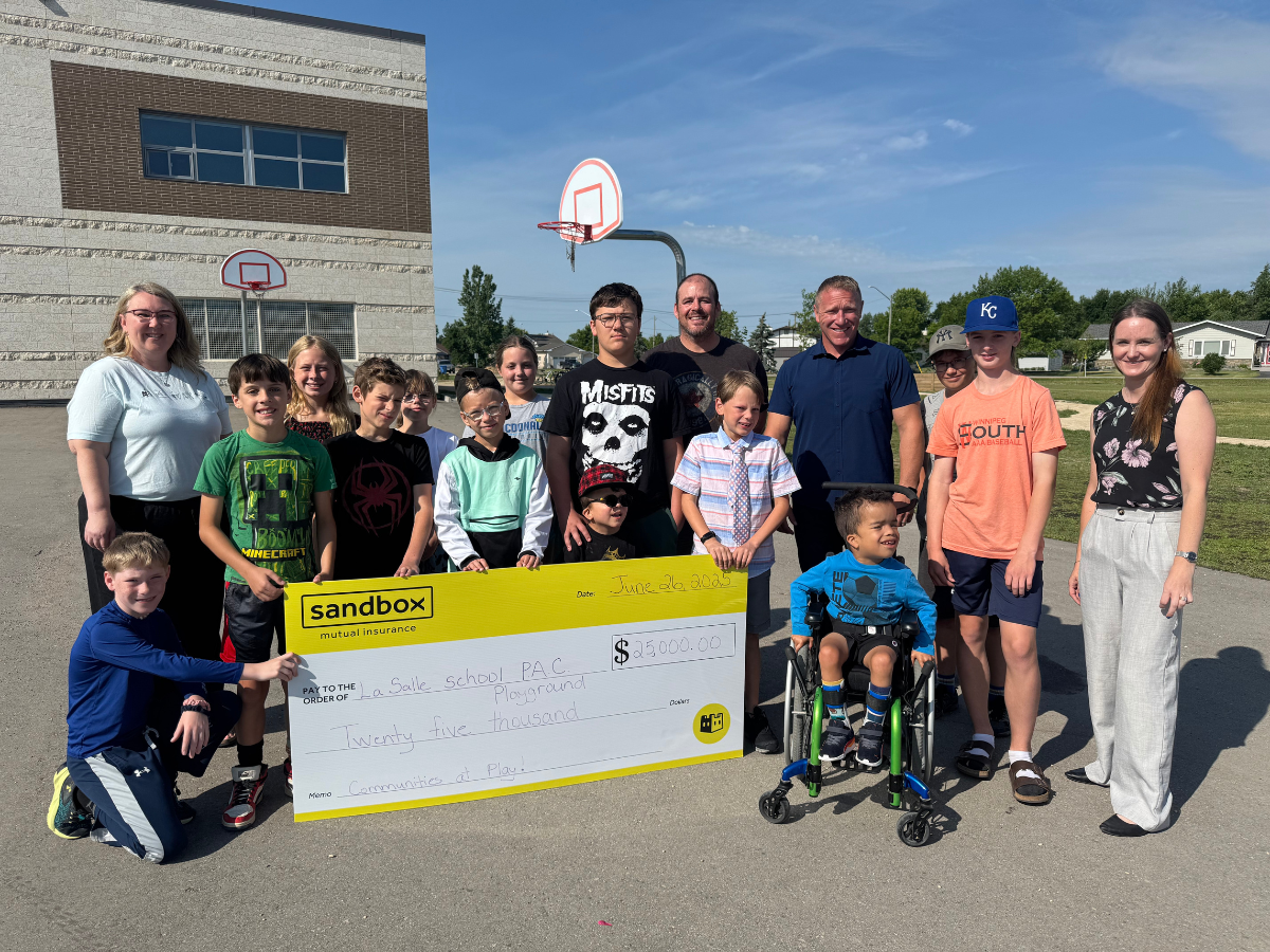Leticia, Manitoba Growth Partner for Sandbox, presents a $25,000 cheque in support of the La Salle School Playground Project, joined by excited students and school staff.