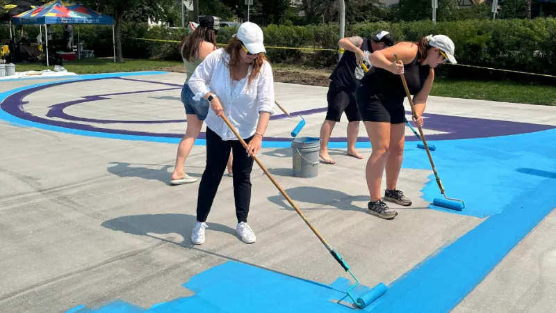 Sandbox Staff members use paint rollers to paint the basketball court.
