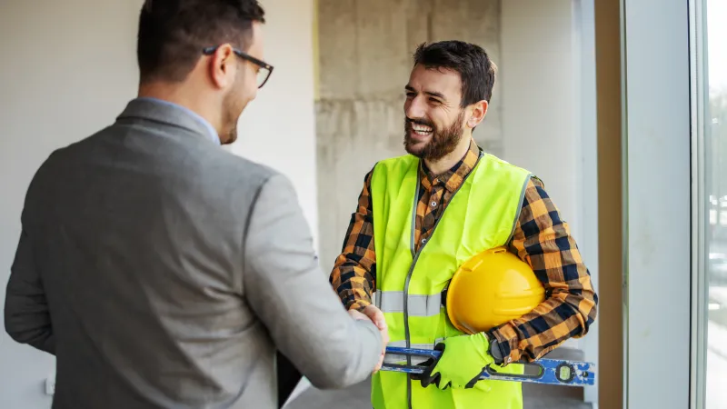 Contractor and project manager shaking hands on a job site while discussing construction plans.