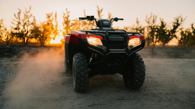 A red Honda ATV parked on a dirt trail at sunset, providing peace of mind with Sandbox ATV insurance coverage.