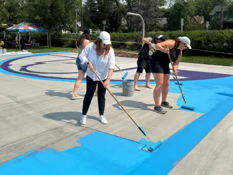 Sandbox Staff members use paint rollers to paint the basketball court.