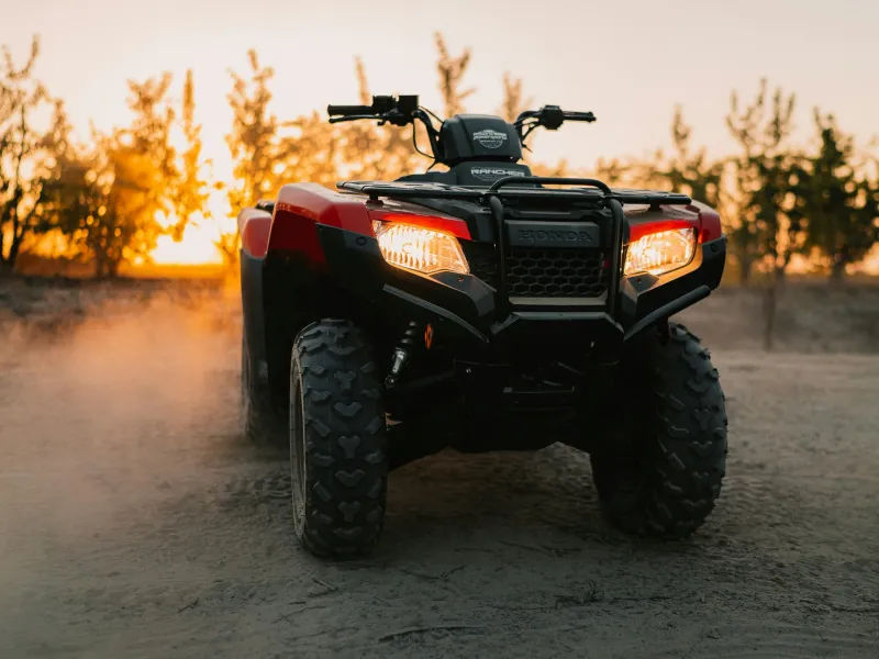 A red Honda ATV parked on a dirt trail at sunset, providing peace of mind with Sandbox ATV insurance coverage.